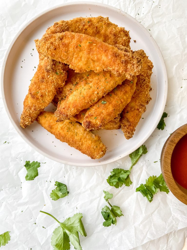 A large plate of golden-brown, paleo chicken tenders with a side of dipping sauce!